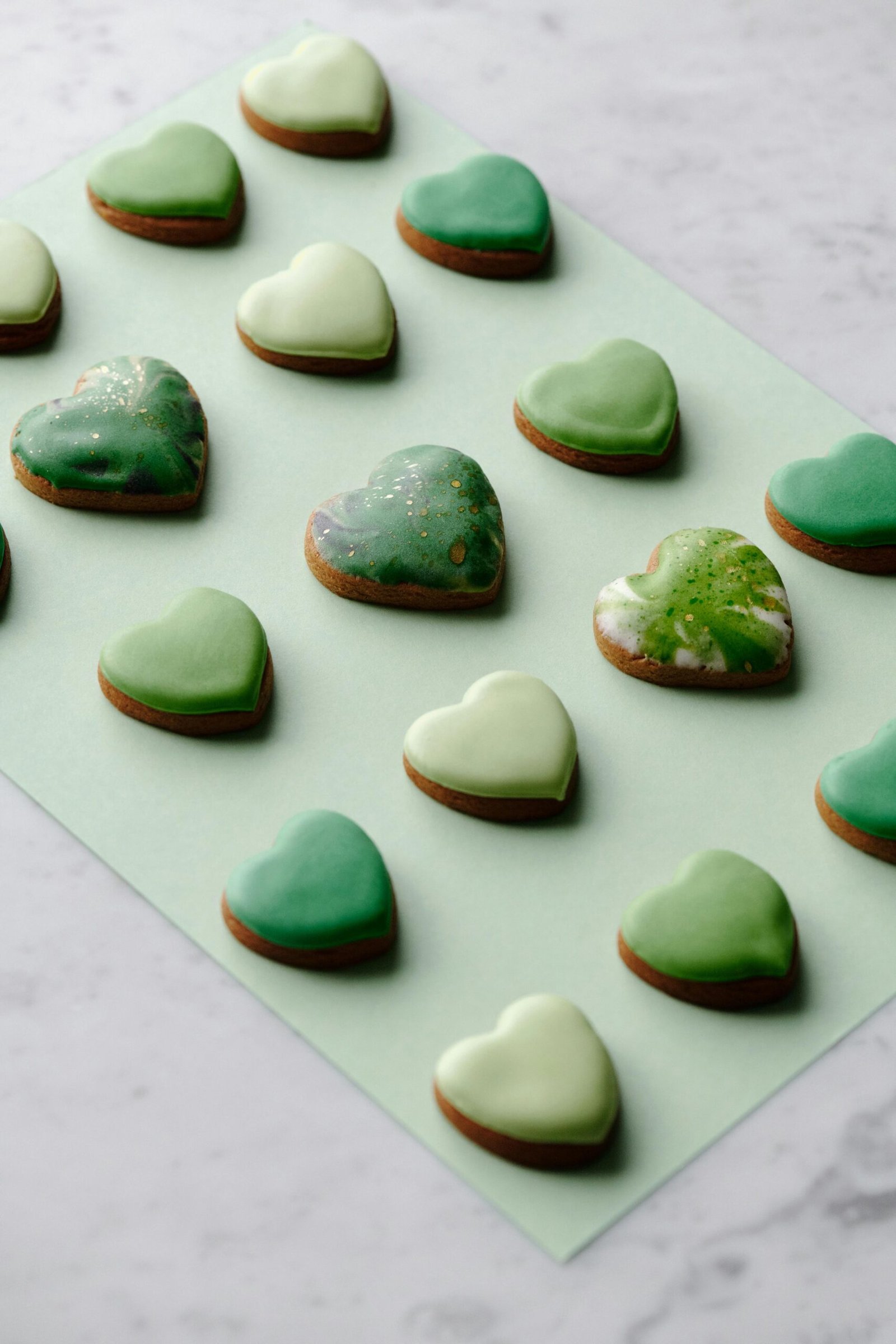A flat lay of green iced heart-shaped cookies on pastel paper, perfect for a sweet treat theme.